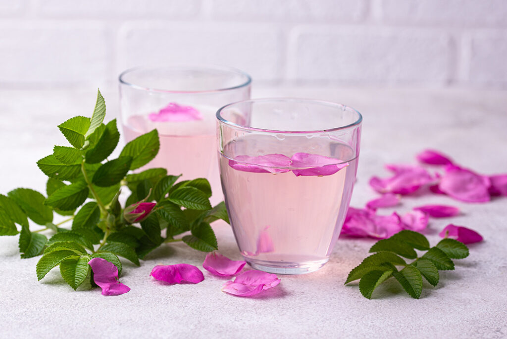 Rosenwasser in einem Glas mit Rosenblüten die oben aufschwimmen.