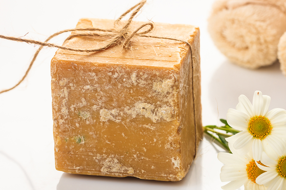 Badekugel zum relaxen. Eine würfelförmige Badekugel aus römischer Kamille. Daneben liegen ein paar Kamille-Blüten.
