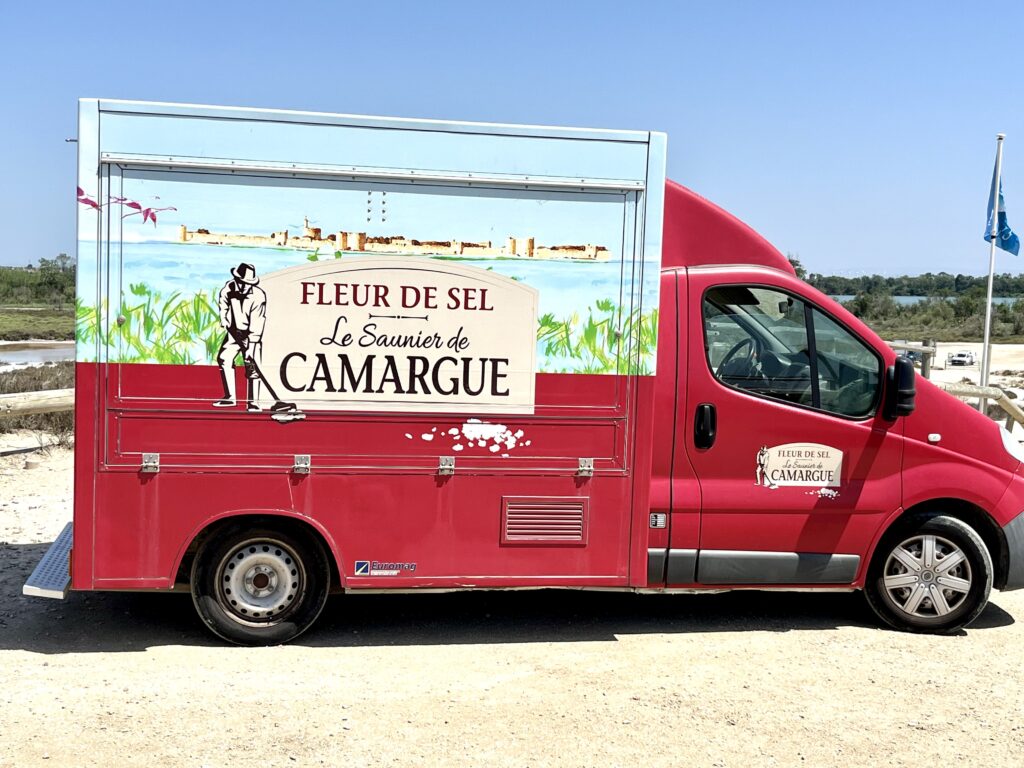Ein roter Lieferwagen mit der Aufschrift "Fleur de Sel - Camargue" in Camargue in der Nähe der Salzfelder, wo Fleuer de Sel hergestellt wird. In der Provence in Frankreich.