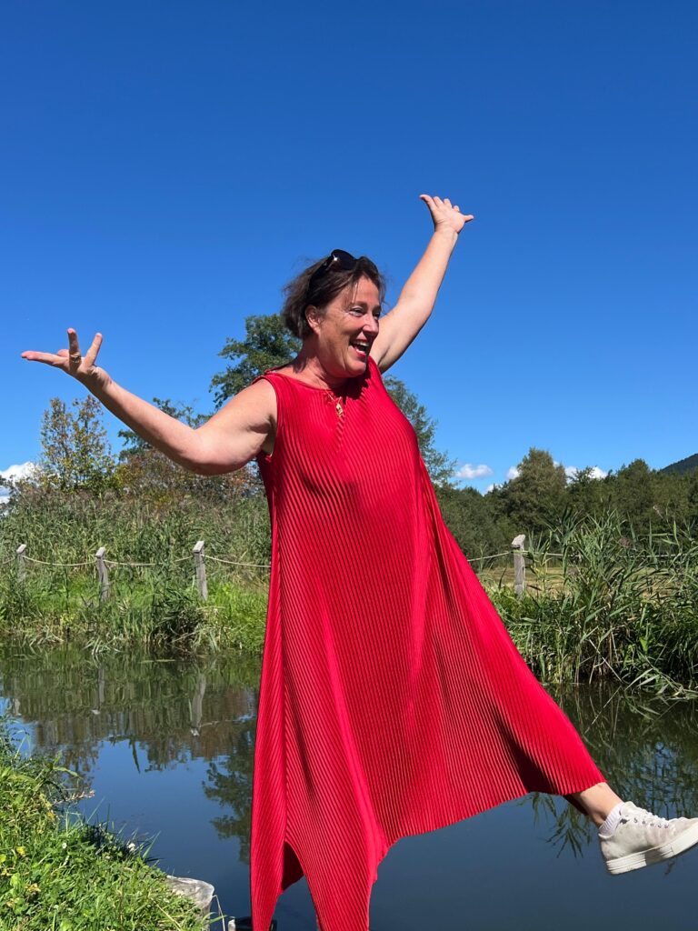 Barbara Tausch im roten Kleid am Wasser als Symbol für Transformation, Lebensfluss und emotionale Balance mit der Tausch-Methode TCTM