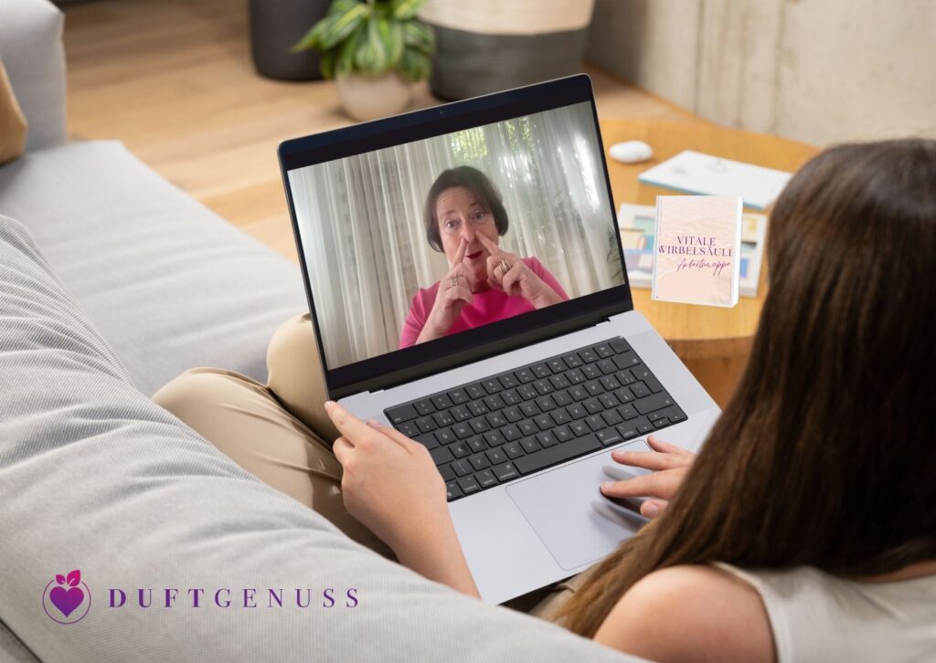 Frau liegt entspannt auf dem Sofa und sieht sich einen Onlinekurs von Duftgenuss auf dem Laptop an. Auf dem Tisch daneben steht das gedruckte Begleitbuch Vitale Wirbelsäule.